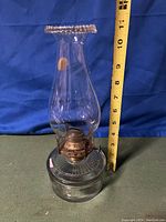 Full view of the vintage oil lamp standing against a blue cloth background with a measuring tape showing 11 inches tall.