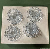 Overhead view of all four teacups and saucers arranged on a white surface showing the translucent blue glass and bubble pattern