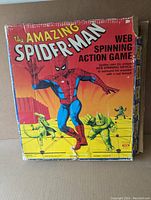 Front of vintage Amazing Spider-Man Web Spinning Action Game box with vibrant artwork showing Spider-Man and villains. Shows wear with tears and tape remnants.