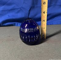 Side view of the cobalt blue glass egg with clear cut design, showing size next to measuring tape approximately 3.5 inches tall.