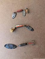 Three fishing lures with metal spinner blades and worn painted bodies, showing signs of use and rust on hooks and connectors.