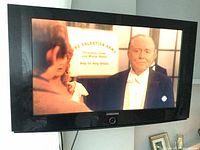 Samsung TV mounted on the wall showing a scene from a movie or show, with visible Samsung logo beneath the screen.