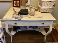 Front view of off white painted antique desk with various small items on top showing surface and drawer details
