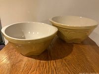 Two yellow ceramic mixing bowls with white interiors placed side by side.