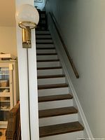 Full view of antique brass wall light fixture mounted beside a staircase, showing the globe light and brass arm.