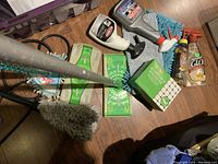 Swiffer sweepers with blue microfiber cloth heads alongside several packs of dry sweeping refill wipes, spray bottles of stainless steel cleaner, and the Amway Glo wooden surface cleaner spray.