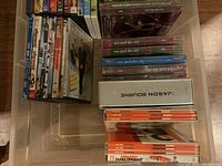 Photo showing DVD cases stacked and lined up including Sex and the City DVDs, Jason Bourne Collection, and other assorted DVDs