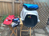 Medium plastic dog crate with front door open, small blue carrying bag on top, and some toys inside the crate.