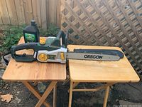 Electric Yardworks chainsaw and bar and chain oil bottle displayed on a wooden table outdoors with a fence in the background.