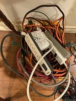 Photo of box filled with tangled extension cords and power bars, showing multiple cords and at least two visible power bars.
