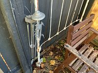 Photo of metal wind chimes with hanging sun and moon decorations beside wooden chair and bench.