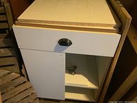 Photo showing closed cabinet with drawer and one door partly open to display interior shelf and metal drawer slides.
