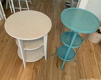 Photo showing two tiered decorative tables, one white wooden with three tiers and one blue painted metal with three tiers.