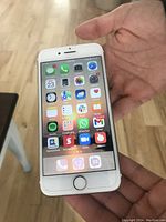 White Apple iPhone held in hand with screen on displaying apps, screen protector visible.