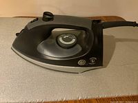 Side view of GE electric iron showing temperature dial and steam knob, power cord visible, resting on small ironing board.