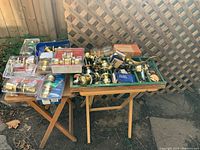 Wide view of lot showing multiple door locks and knobs spread across two tables outdoors, including both packaged and loose items in brass finish.