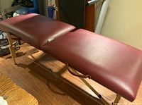 Maroon cushioned massage table unfolded and set up, showing surface and legs.