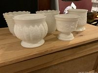 Front angle view of five milk glass containers displaying varying textures and shapes on a wooden table.