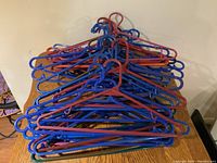 Photo showing a large pile of mixed blue and red plastic clothes hangers stacked on a wooden surface against a white wall.