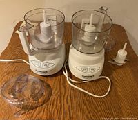 Two Cuisinart Mini-Prep Plus choppers with clear plastic bowls, lids, and blades on wooden table.