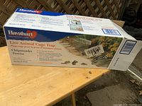 Photo of the Hevalhart branded live animal cage trap box featuring product information and pictures of target animals such as chipmunks and tamias. Shows the box with brand logo, model number 0745, and uses in multiple languages.