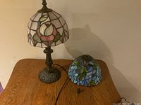 Full view of stained glass lamp with primary floral shade on the base and extra blue stained glass shade lying on the table.