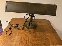 Front view of vintage adjustable desk lamp on wooden table showing base, arm, and copper-colored shade.