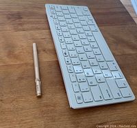 White wireless keyboard and silver Jot Pro stylus pen placed side by side on a wooden surface.