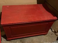 Front view of red painted wooden storage box showing rectangular shape and panel design with rounded feet