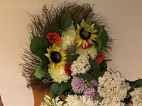 Photo showing the spring-themed wreath composed of sunflowers, large hydrangea flowers, red poppies, and green leaves on a twig base