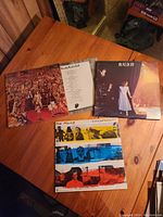 Photo showing three vinyl albums displayed on a wooden table: The Rolling Stones, Rush, and The Police Synchronicity.