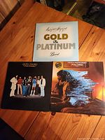 Photo shows three vinyl record albums laid out on a wooden table: 'Lazy and Hazy and Gold & Platinum Band', 'Alfredo Socarro & Manolito Simonet', and 'The Alan Parsons Project Pyramid'.