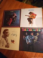Four vinyl album covers displayed on a wooden table: Janis Joplin's "Pearl", a Jimi Hendrix acoustic guitar cover, Jimi Hendrix's "The Cry of Love", and The Jimi Hendrix Experience's "Smash Hits"