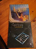 Two Supertramp vinyl album covers: 'Breakfast in America' on top and 'Crime of the Century' underneath on a wooden surface.