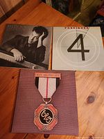 Photo showing the front covers of two vinyl vinyl record albums and a music-themed medal plaque with the ELO logo.