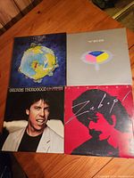 Photo displaying four vintage vinyl albums by Yes, George Thorogood, Santana, and an illustrated globe-themed record