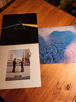 Three Pink Floyd LP albums on a wooden table: Dark Side of the Moon, Wish You Were Here, and Meddle albums visible with distinct cover arts.