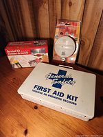 Closed view of General Safety First Aid Kit, Survival Kit box, and Barnson smoke detector still in packaging on wooden surface.