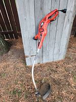 Full view of the Black and Decker electric string trimmer showing orange handle, curved metal shaft, and cutting head with shield.