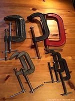 Photo shows five assorted size C-clamps on a wooden surface, colors include grey, black, and red.