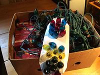 Photo of a box filled with bundled Christmas light strands and several replacement bulbs organized on a white card in red, blue, yellow, and green colors.