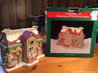 Porcelain candy-themed illuminated Christmas house next to box labeled Deer Depot with image of the house on the box.