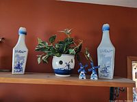 Shelf display of two white ceramic decanters with blue Dutch windmill paintings, a blue and white ceramic planter with a plant, and a pair of blue windmill salt and pepper shakers.