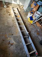 Full view of the large aluminum extension ladder lying on a concrete floor in a garage setting showing rungs and locking mechanisms.