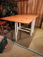 Wooden folding IKEA table shown open with visible wood grain and white legs against wood paneled background.