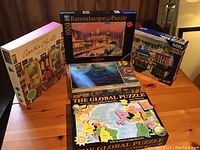 Lot of 5 puzzles on wooden table, showing puzzle boxes mostly unopened
