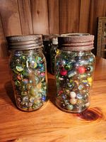 Photo of two Canadian Jewel glass jars filled with multi-color vintage marbles on wooden surface.