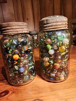 Two large vintage Mason jars filled with various multi-colored glass marbles with rusted lids