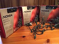 Four boxed sets of NOMA indoor mini Christmas lights on wooden surface, three blue and one clear.