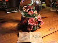 View of the musical globe showing the glass sphere with a hummingbird and flowers inside, and a base decorated with pink flowers.